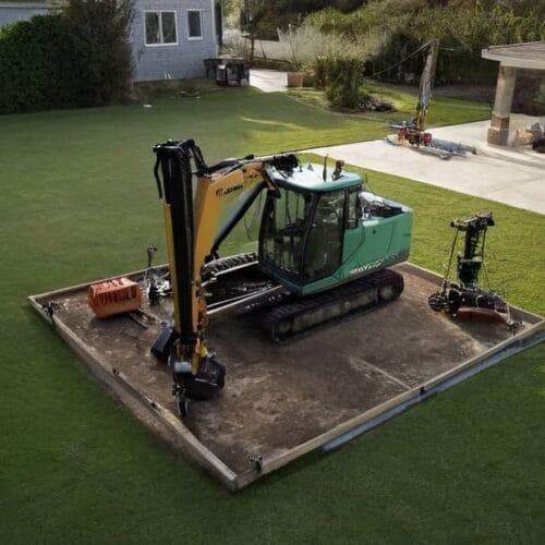 Mały dom jednorodzinny na zielonej działce oraz sprzęt do wiercenia studni głębinowej przygotowany do pracy w naturalnych warunkach.