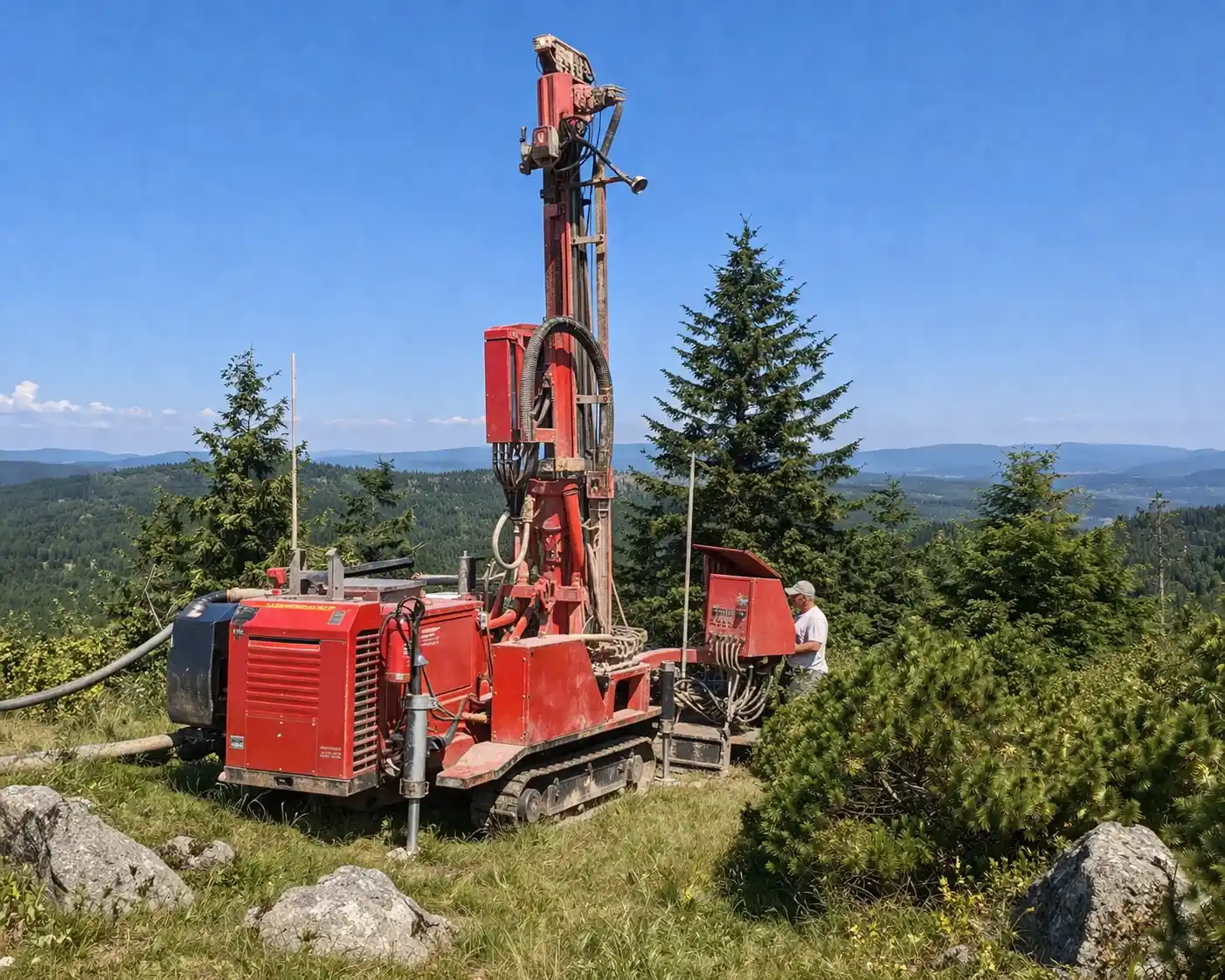 Czerwona wiertnica wykonująca studnie głębinowe w Brennej na górskim terenie wśród lasów i skał